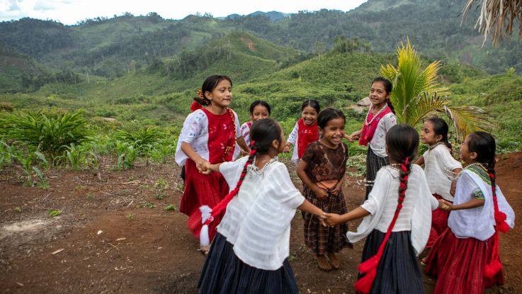 Girls in traditional dress laughing and playing games outside a homestead during ActionAid's annual child message collection, in Semanzana.