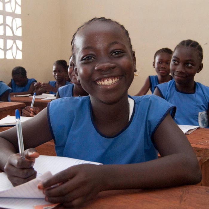 Smiling girl Kadiatu Sesay wearing blue school uniform sitting at her desk in a classroom at Kola Tree Community School, Western Area, Sierra Leone