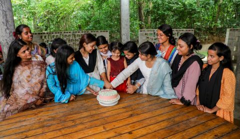 Girls sat around a table and cutting a cake in Bangladesh