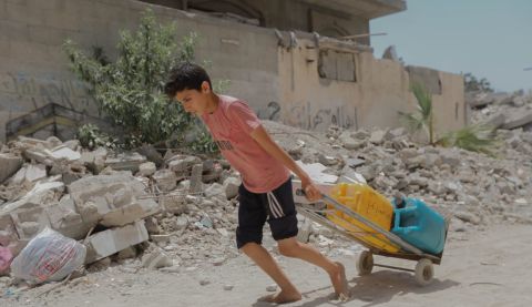 Boy wheeling water cans in Gaza