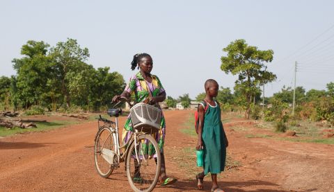 A woman and her daughter walking to school and holding a bike