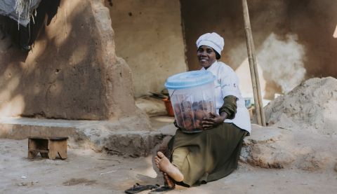 woman in a chef uniform holding a basket opr tub of food