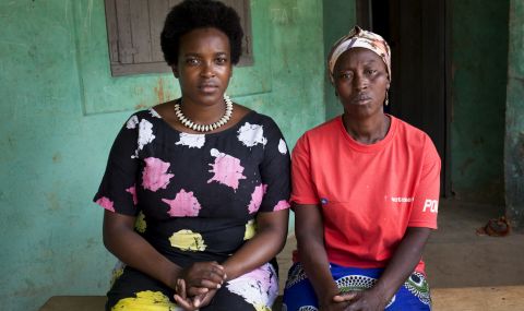 Wunmi Mosaku (left) wearing patterned shirt and skirt sitting on a bench with a Ghanian woman wearing ActionAid T shirt in rural Ghana