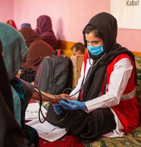 A midwife wearing mask holding stethoscope sitting in mobile health unit surrounded by women Afghanistan