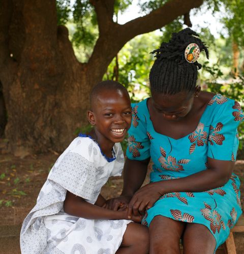Elizabeth helps her daughter Eunice with her homework under a tree behind their house in Ghana