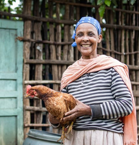 Woman smiling and holding a hen in her hands.