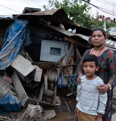 Woman standing outside her destroyed home in Nepal with her son