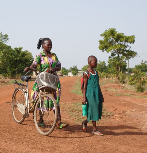 A woman and her daughter walking to school and holding a bike