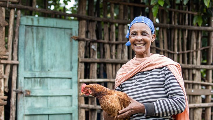 Woman smiling and holding a hen in her hands.