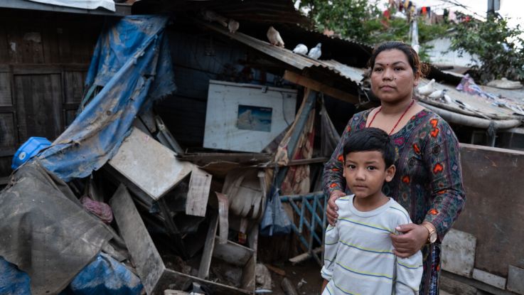 Woman standing outside her destroyed home in Nepal with her son