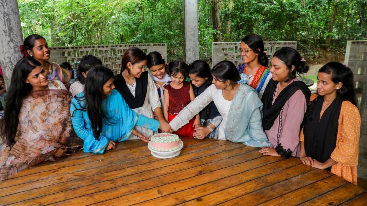 Girls sat around a table and cutting a cake in Bangladesh