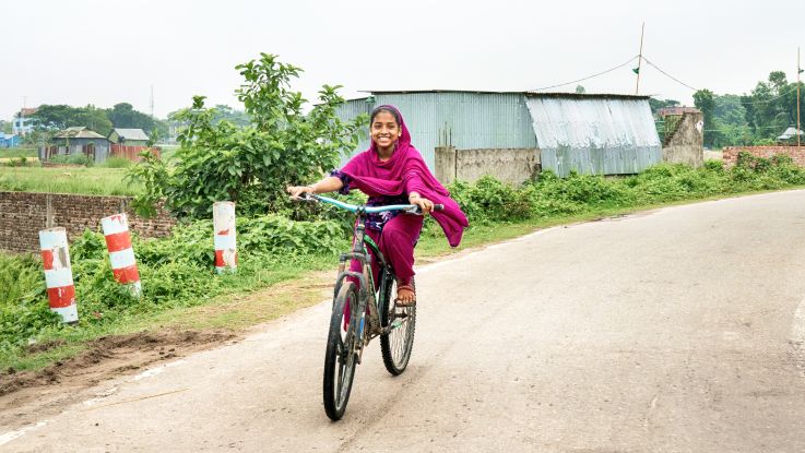 Girl on her bike smiling happily in Bangladesh.