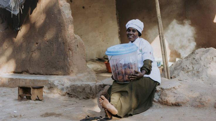 woman in a chef uniform holding a basket opr tub of food